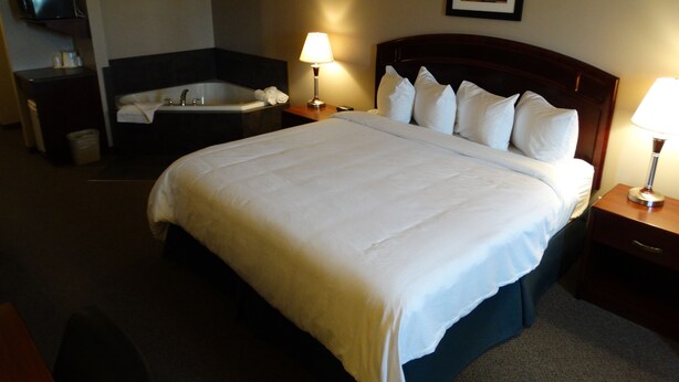 A hotel room with a large bed, a bathtub, a flat-screen TV, and a framed picture on the wall. - R&R Inn (Provost)