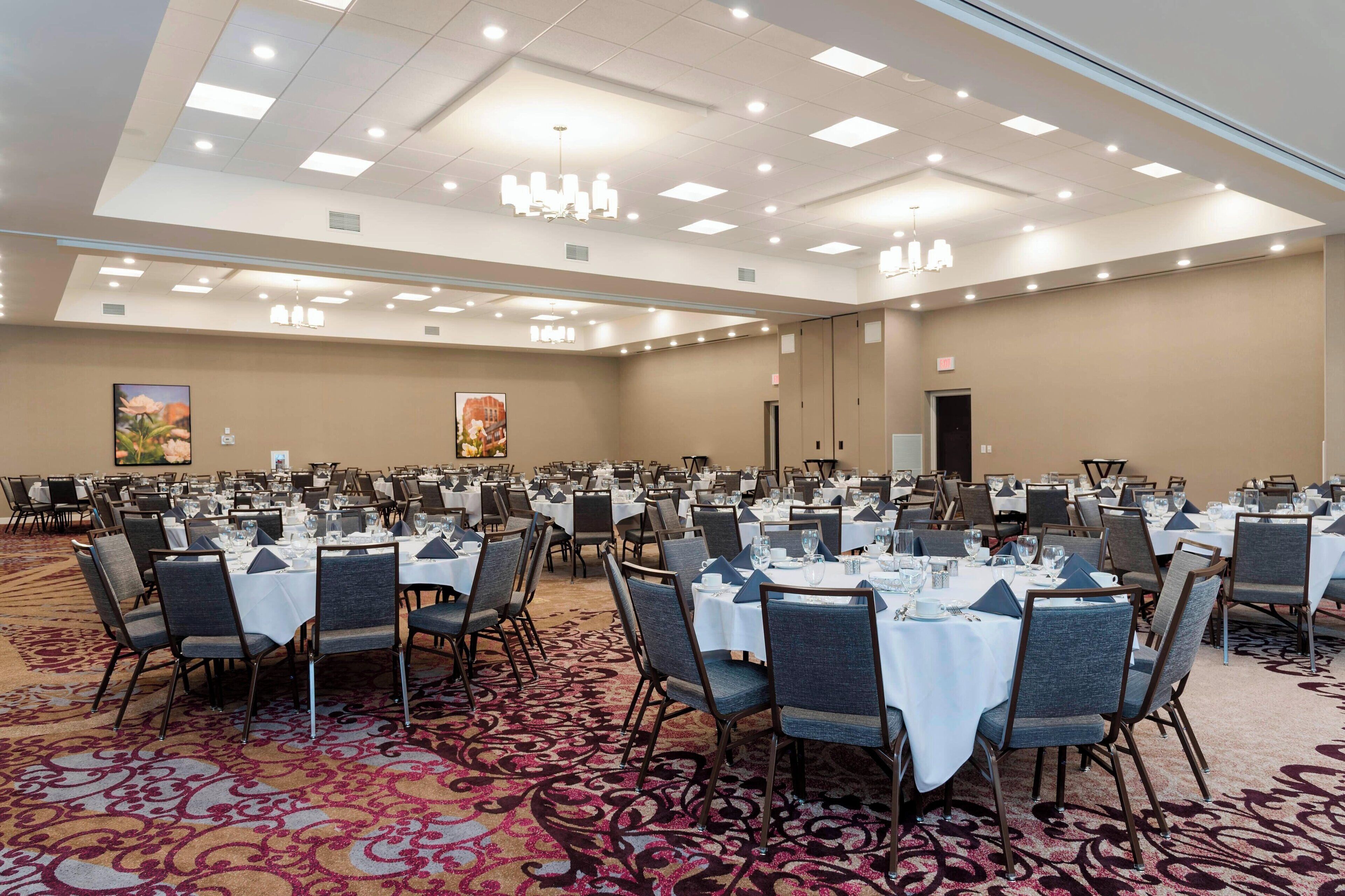 A large banquet hall with multiple round tables set for dining, equipped with chairs and table settings.
