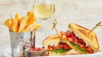 Un sándwich de tocino, tomate y lechuga, una copa de vino blanco y un recipiente de papas fritas.