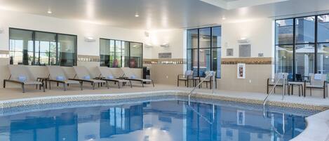 An indoor swimming pool with lounge chairs and a lifeguard on duty sign.