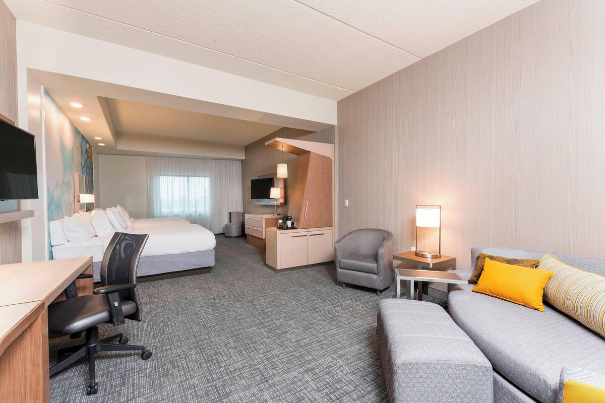 A hotel room with a bed, a desk, a chair, a sofa, and a TV.