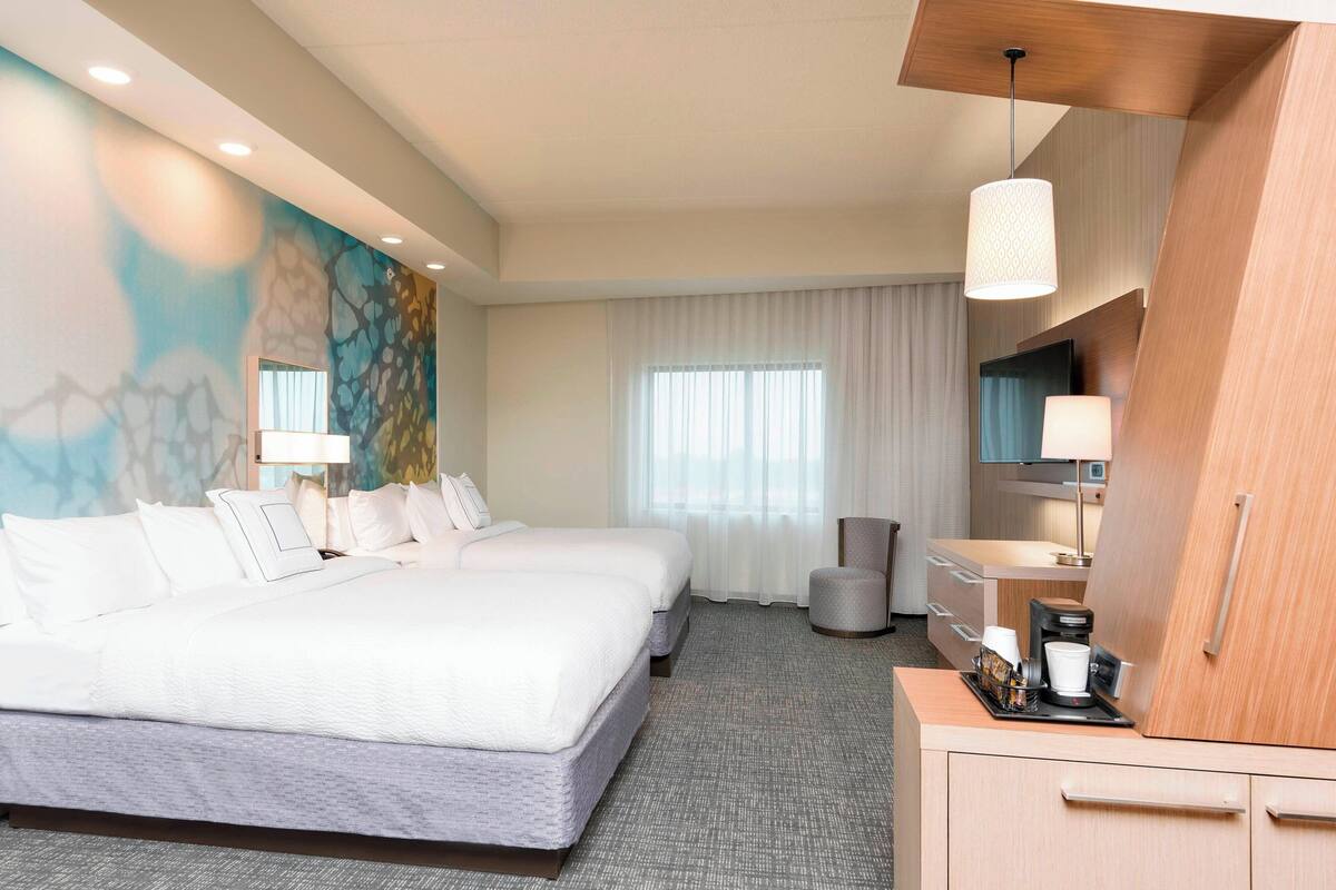 A hotel room with a large bed, a desk with a coffee maker, a TV, and a painting on the wall.