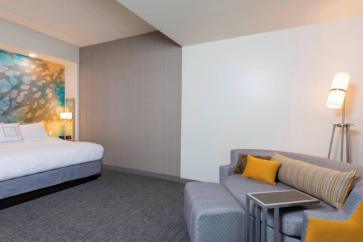 A hotel room with a bed, a sofa, a small table, and a lamp.