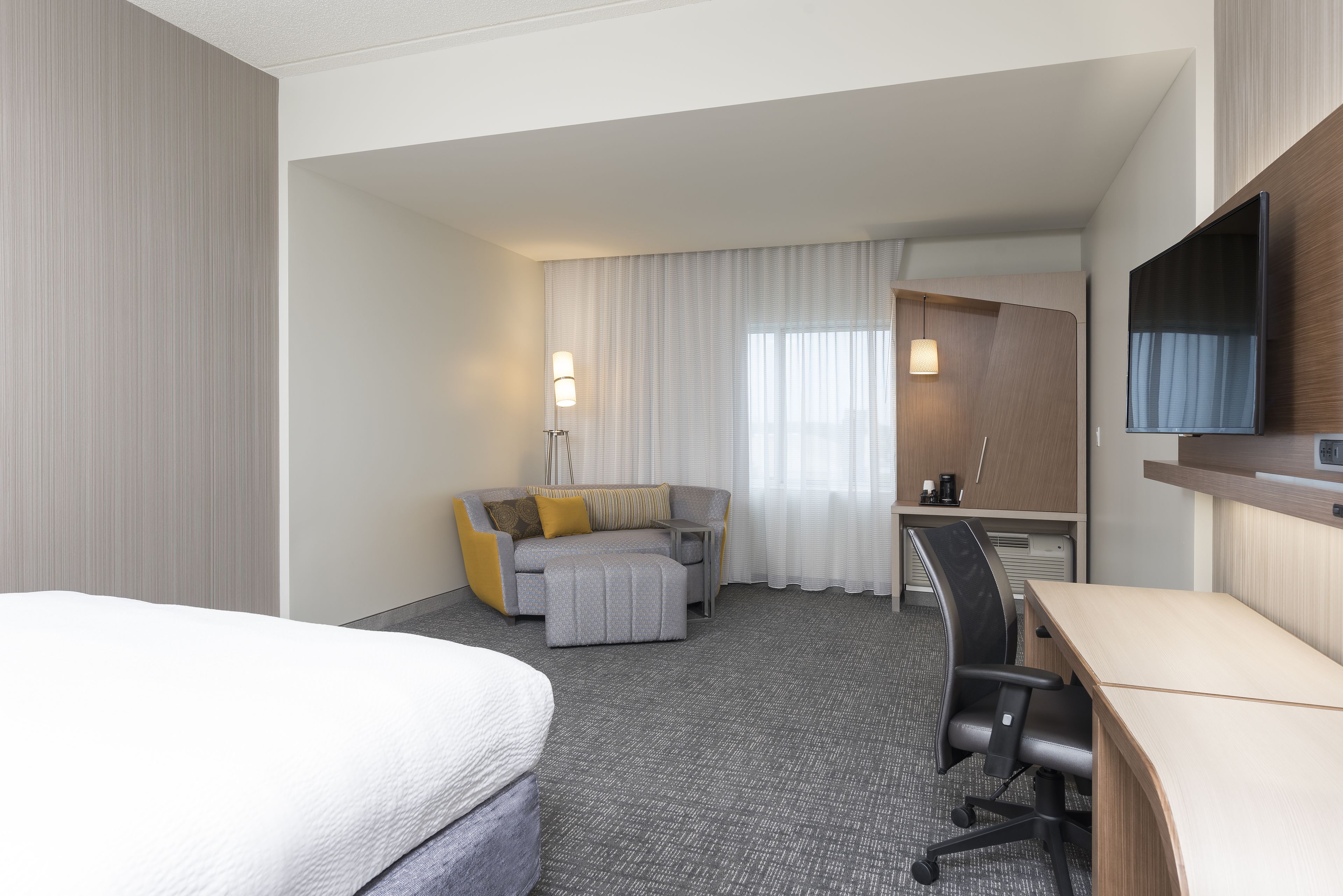 A hotel room with a bed, a sofa, a desk, and a television.