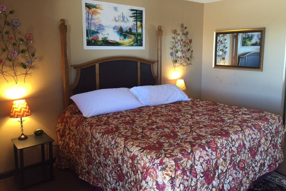 A neatly made bed with a floral bedspread, a wooden headboard, and two bedside lamps.