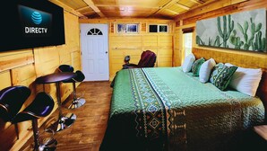 Une pièce de style cabane en bois comprenant un lit, un coin bar avec des tabourets, un téléviseur fixé au mur et une porte.