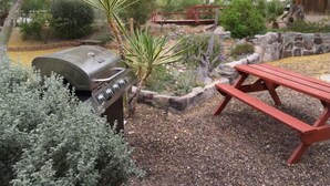 Un barbecue, une table de pique-nique et un jardin agrémenté de diverses plantes et d’un mur en pierre.