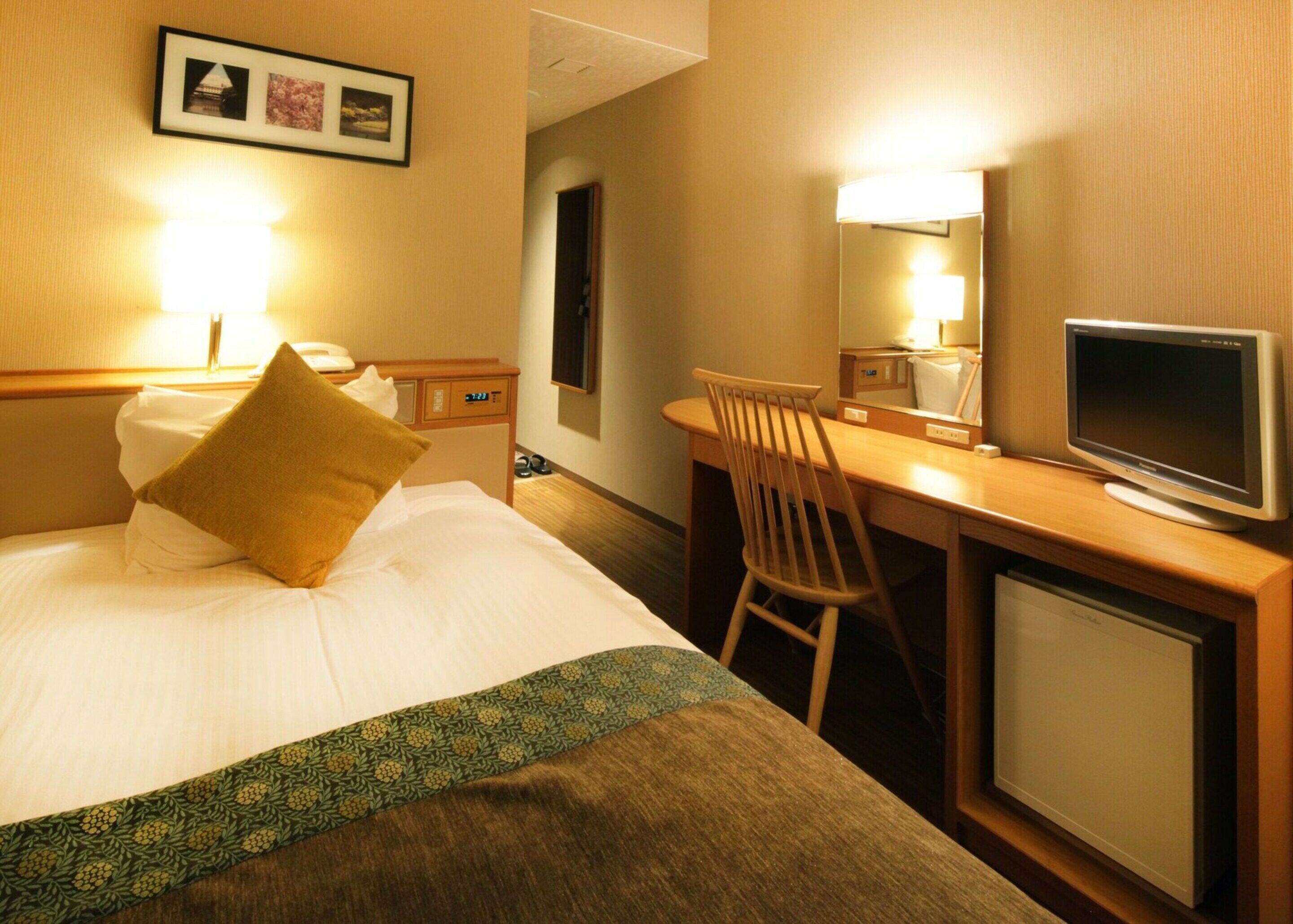 A hotel room with a bed, a desk, a chair, a television, and a mirror.