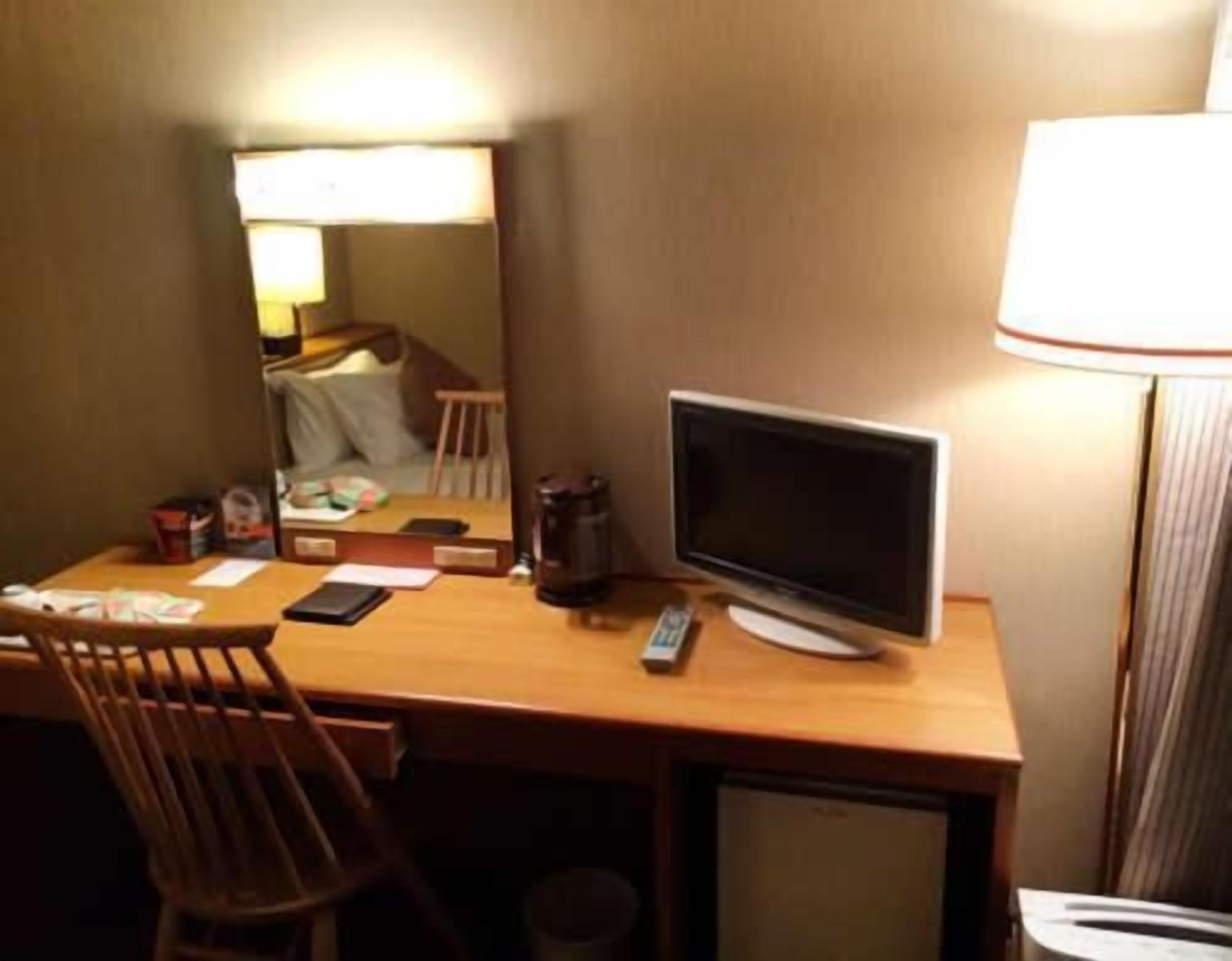Une chambre d’hôtel équipée d’un bureau en bois, d’une télévision, d’une lampe, d’une chaise et d’un petit réfrigérateur.