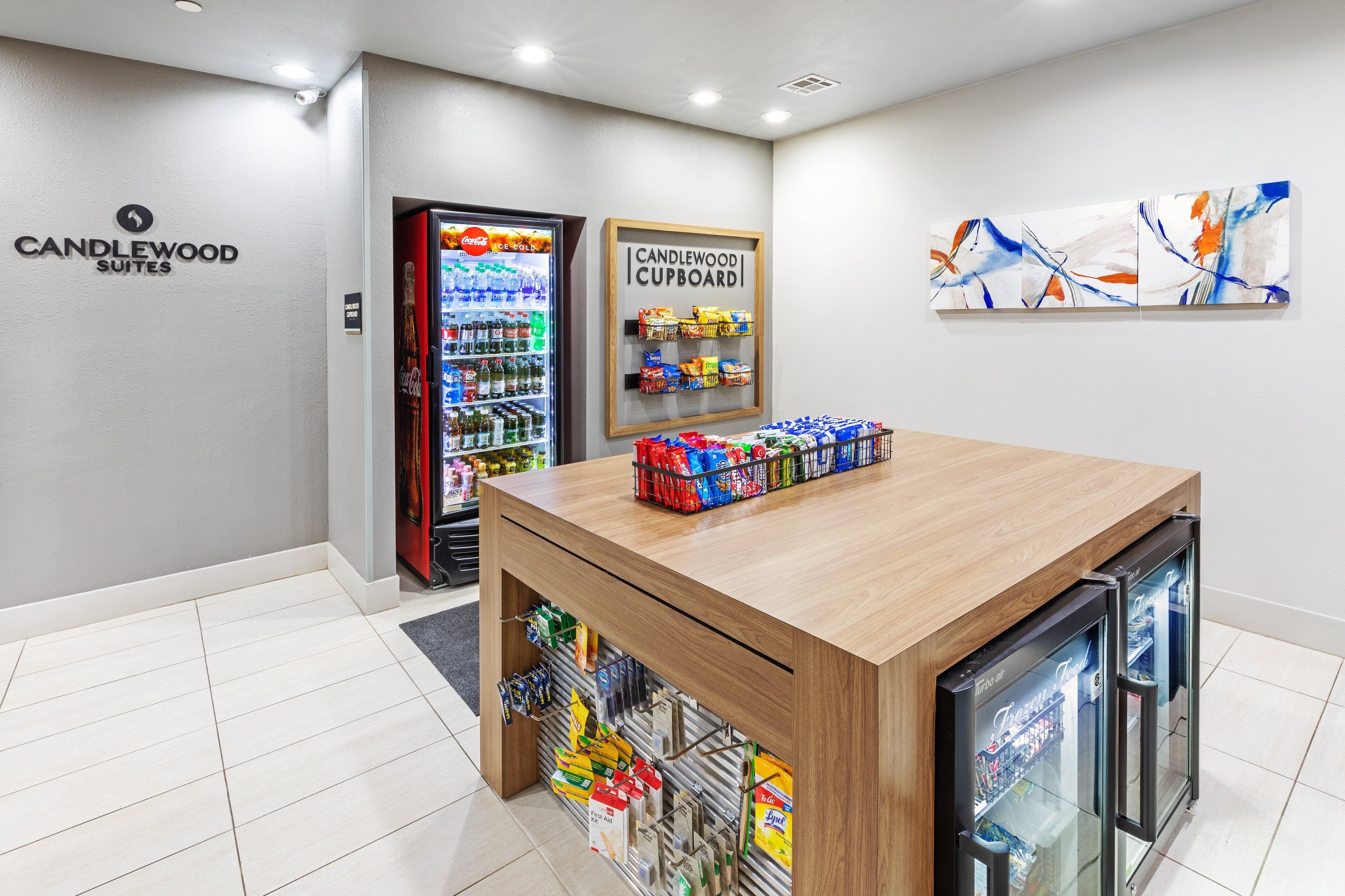 Zona de recepción de un hotel con un mostrador de madera, una vitrina refrigerada y un letrero en la pared para Candlewood Suites.