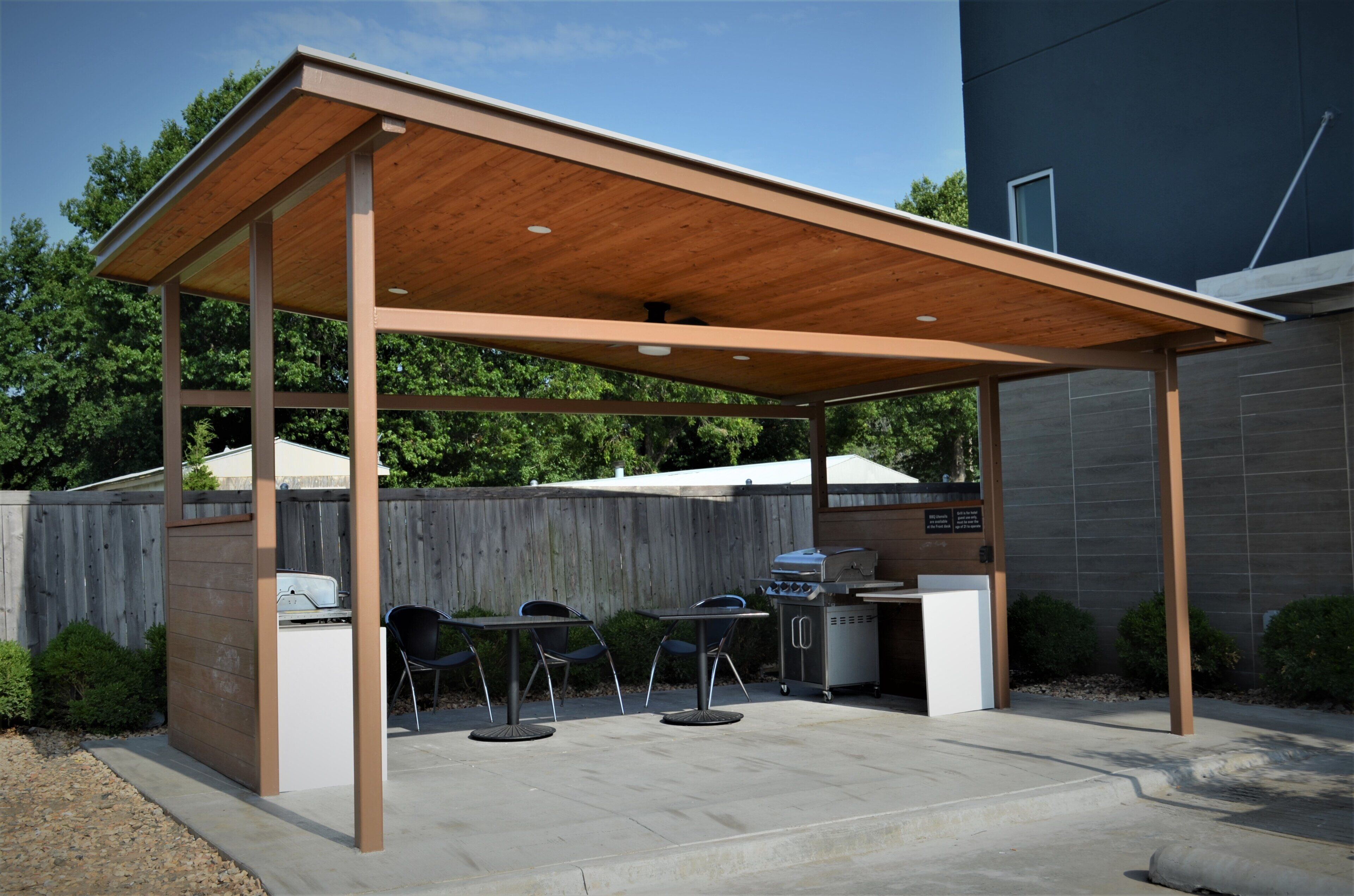 Un patio exterior con techo de madera, una parrilla y asientos.