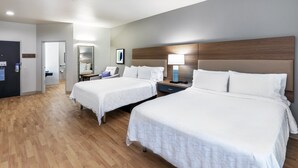Habitación de hotel con dos camas, suelo de madera, una mesita de noche con lámpara y un espejo.