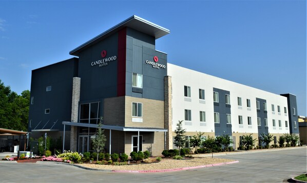 A hotel with a modern design, featuring a prominent 'CANDLEWOOD SUITES' sign, a covered entrance, and a parking area with landscaping.