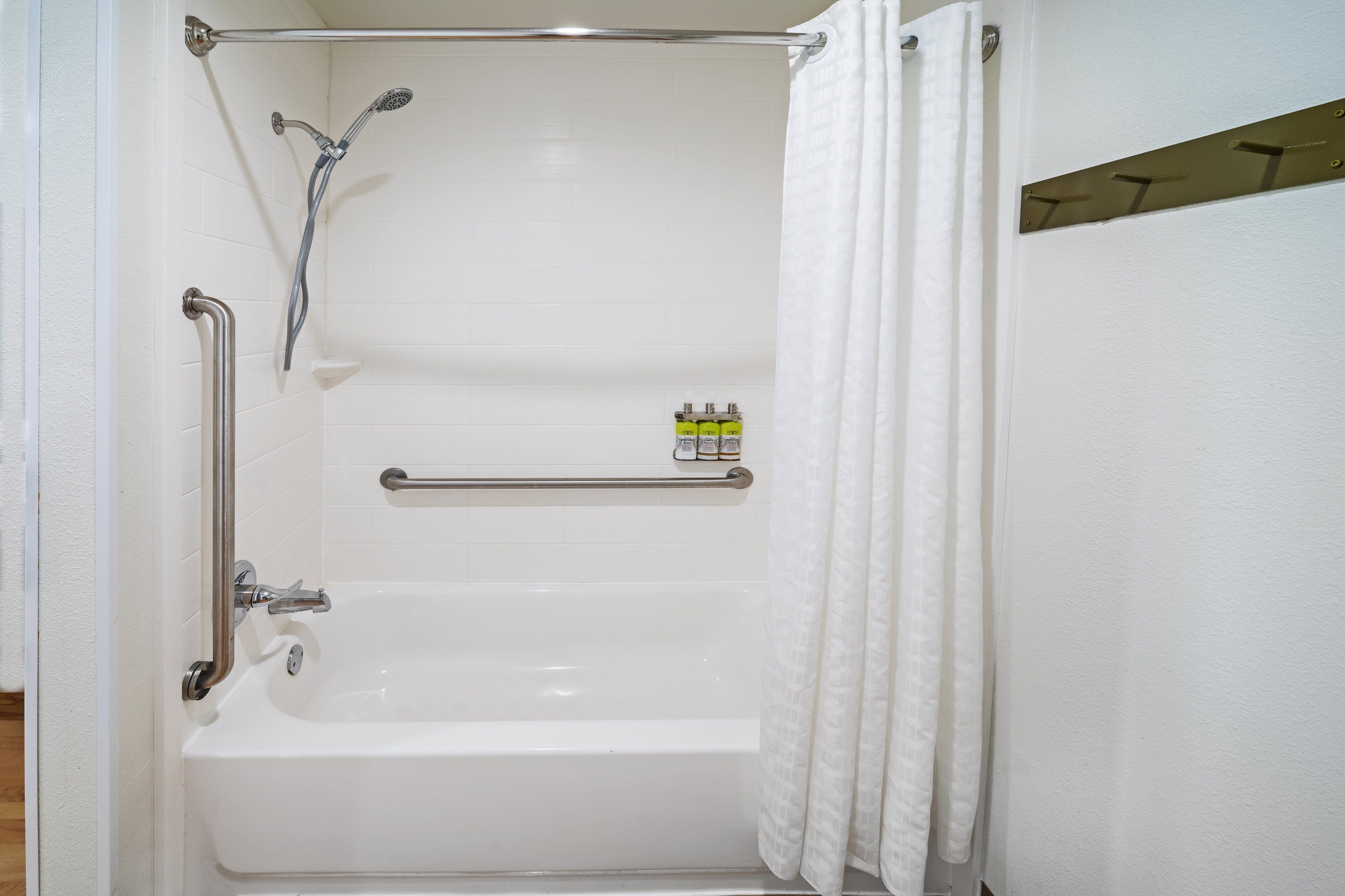 Ducha a ras de suelo con barra de apoyo, cabezal de ducha de mano y estante con artículos de aseo.