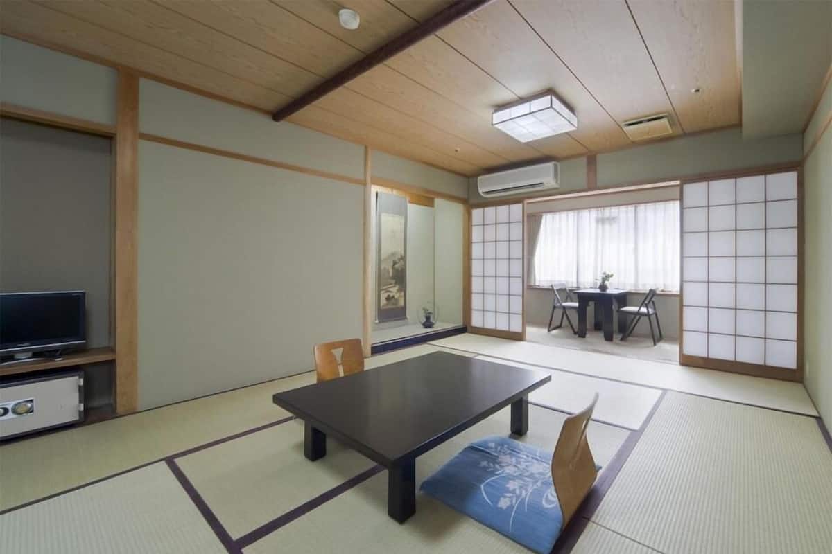 A traditional Japanese room with tatami flooring, a low table, chairs, a television, and a sliding door.