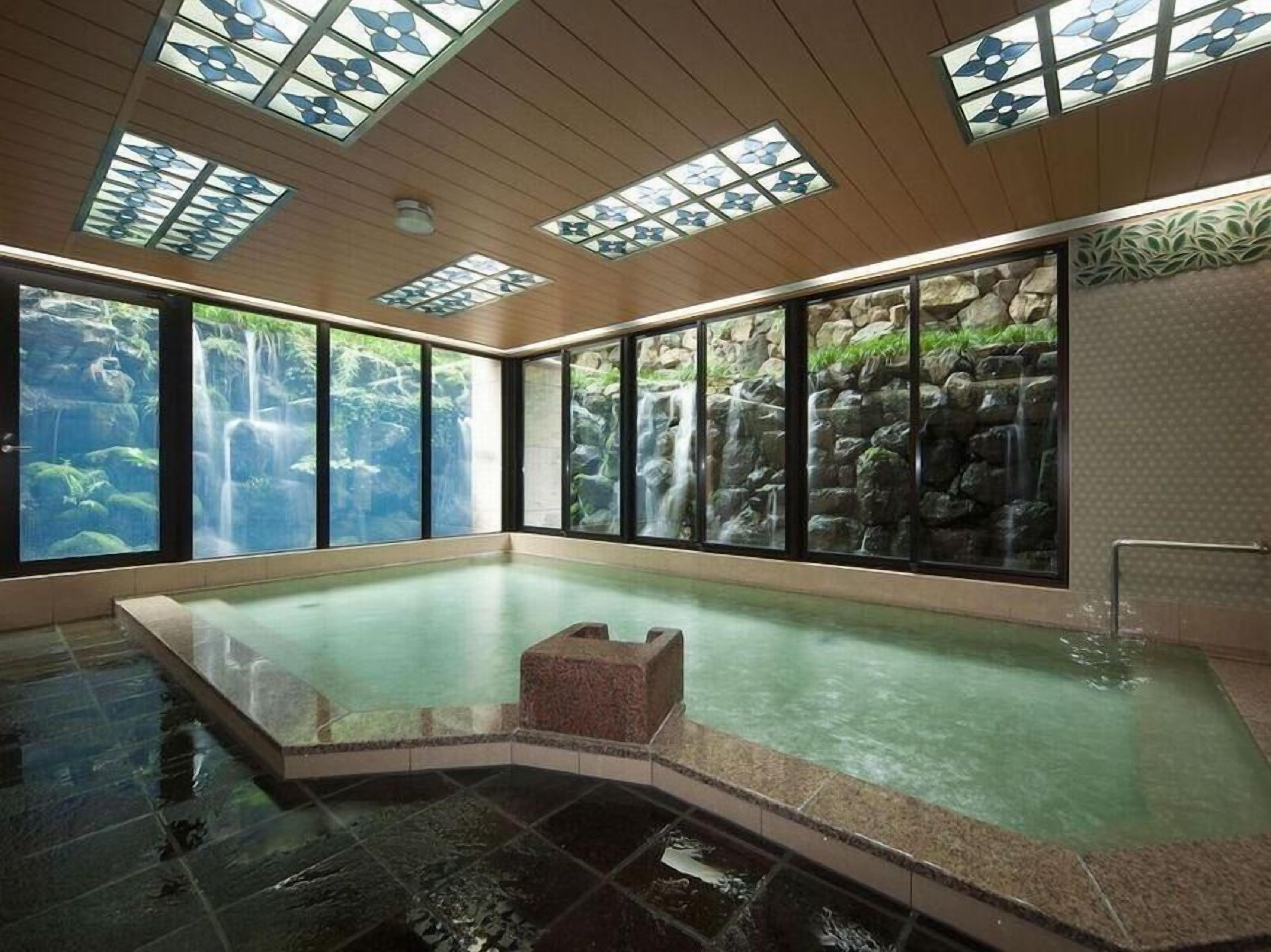A large indoor swimming pool with a waterfall view, wooden ceiling, and large windows.