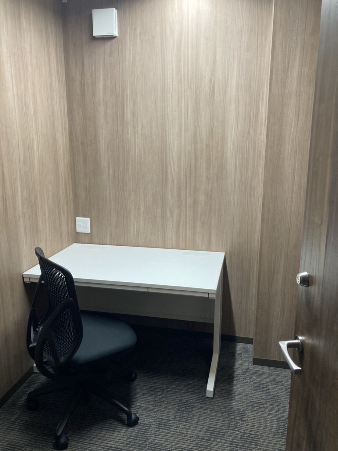 A small office space with a white desk, a black office chair, and a door.