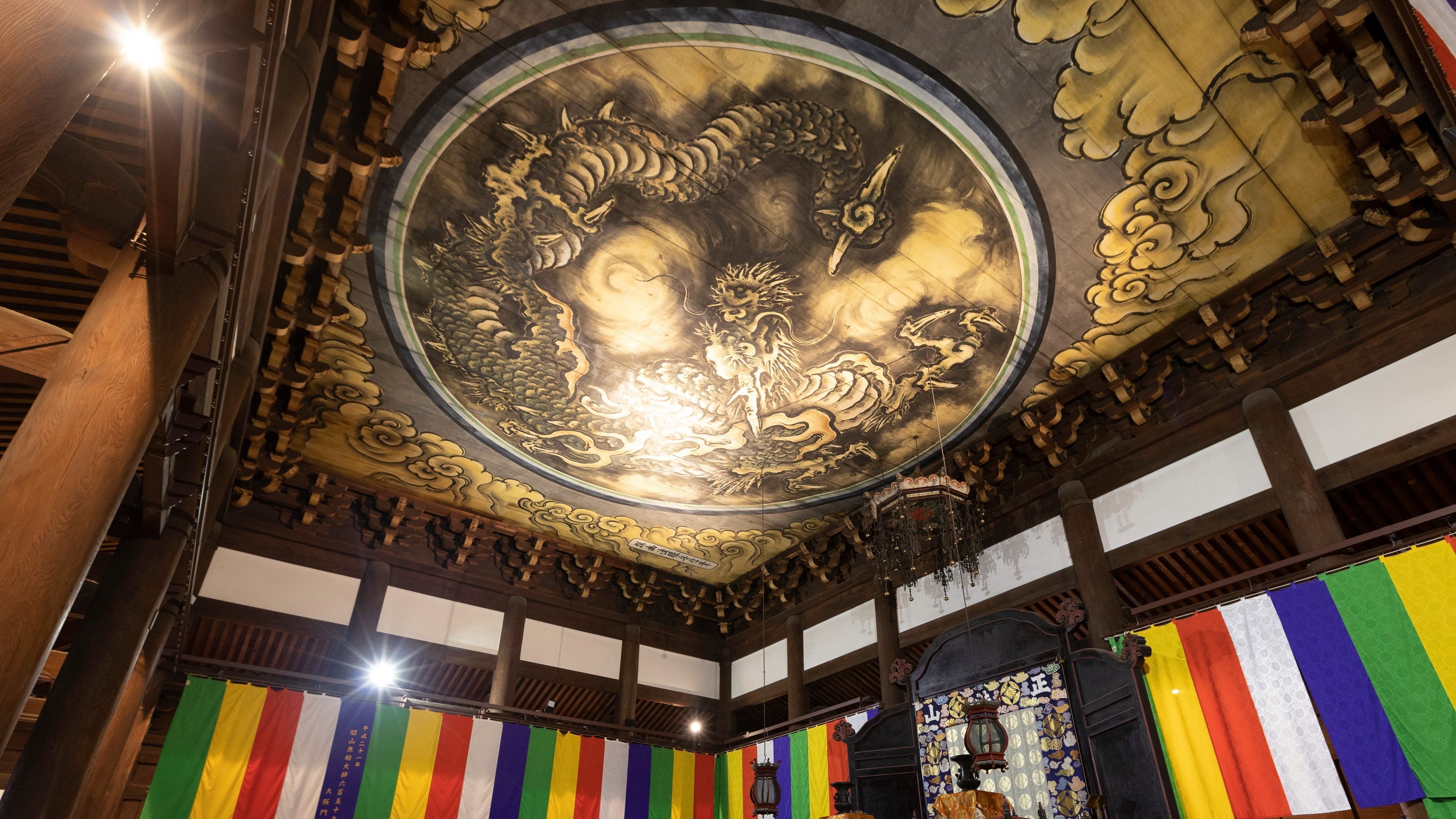 A traditional building interior with a large circular mural on the ceiling, wooden beams, and colorful banners.