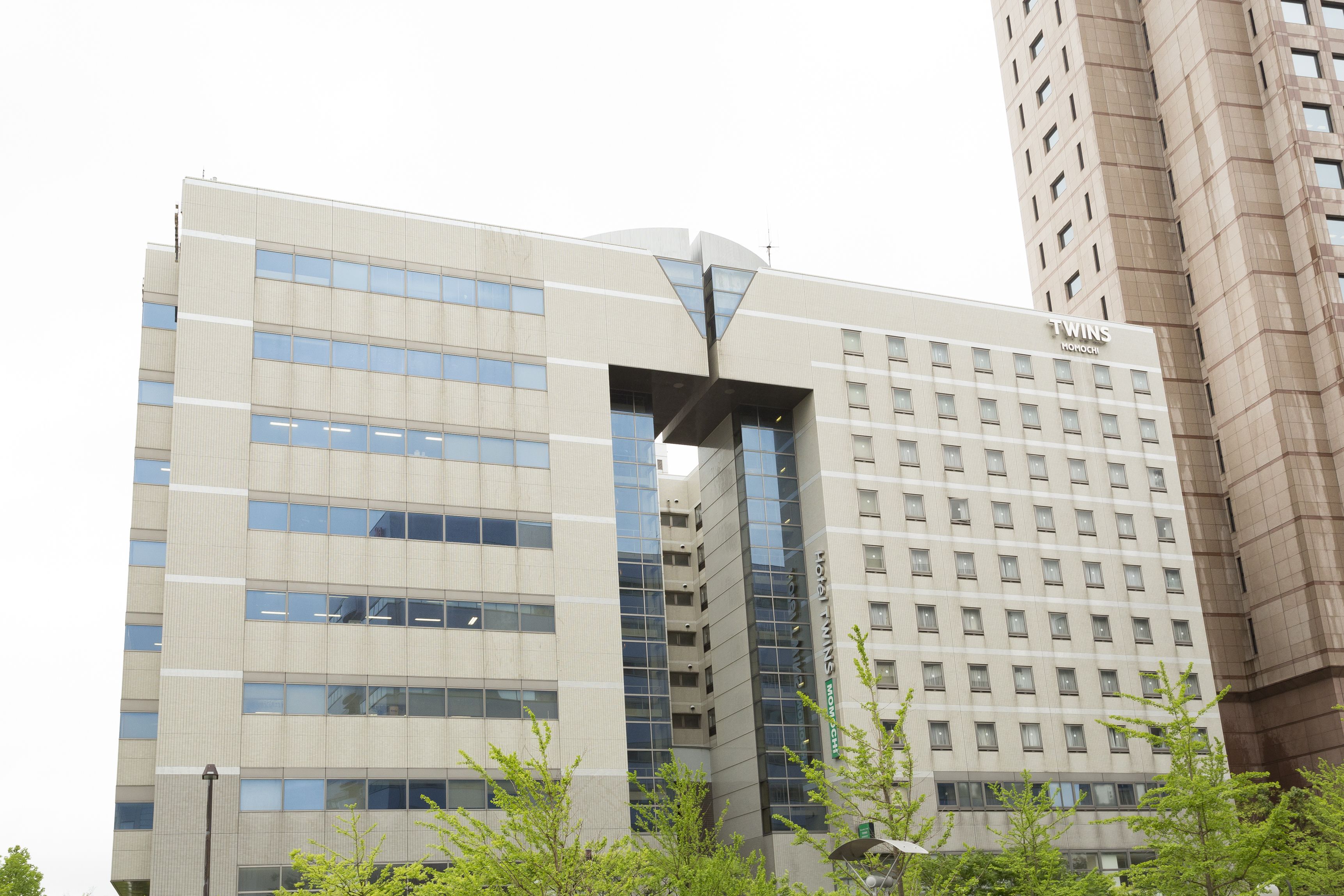 A modern hotel building with a prominent entrance, multiple floors, and a clear view of the interior through the windows.