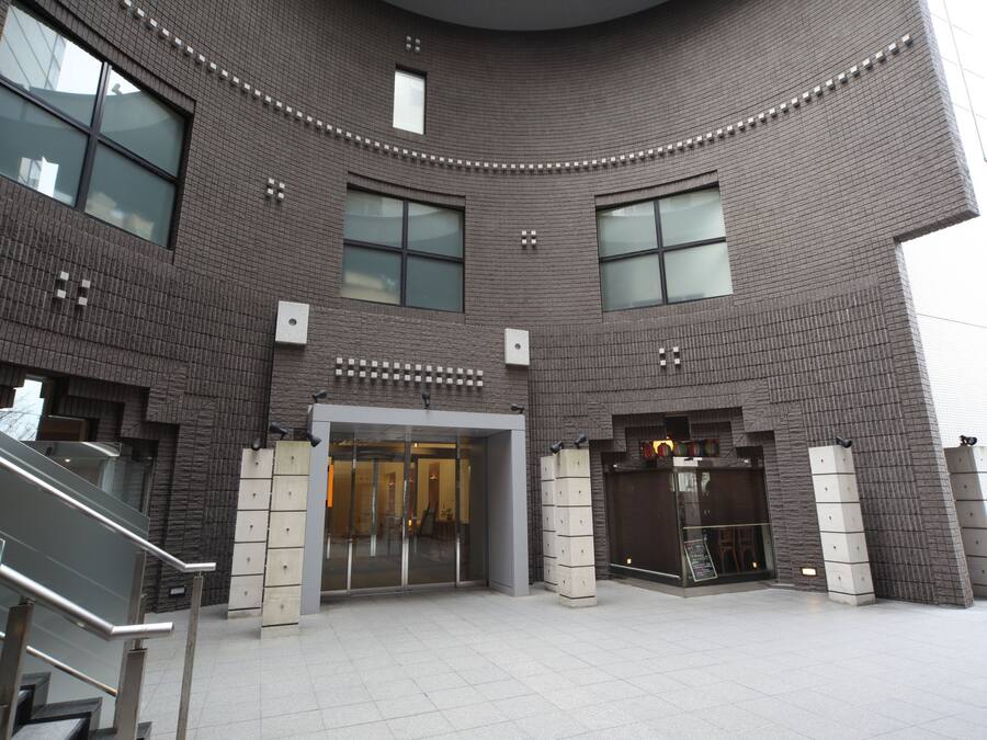 Un edificio moderno con fachada curva, ventanas amplias y una entrada central con puertas de cristal.