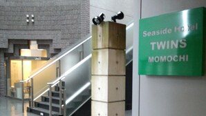 Naamplaat Seaside Hotel Twins Momochi in een moderne lobby met een trap en een structuurwand.