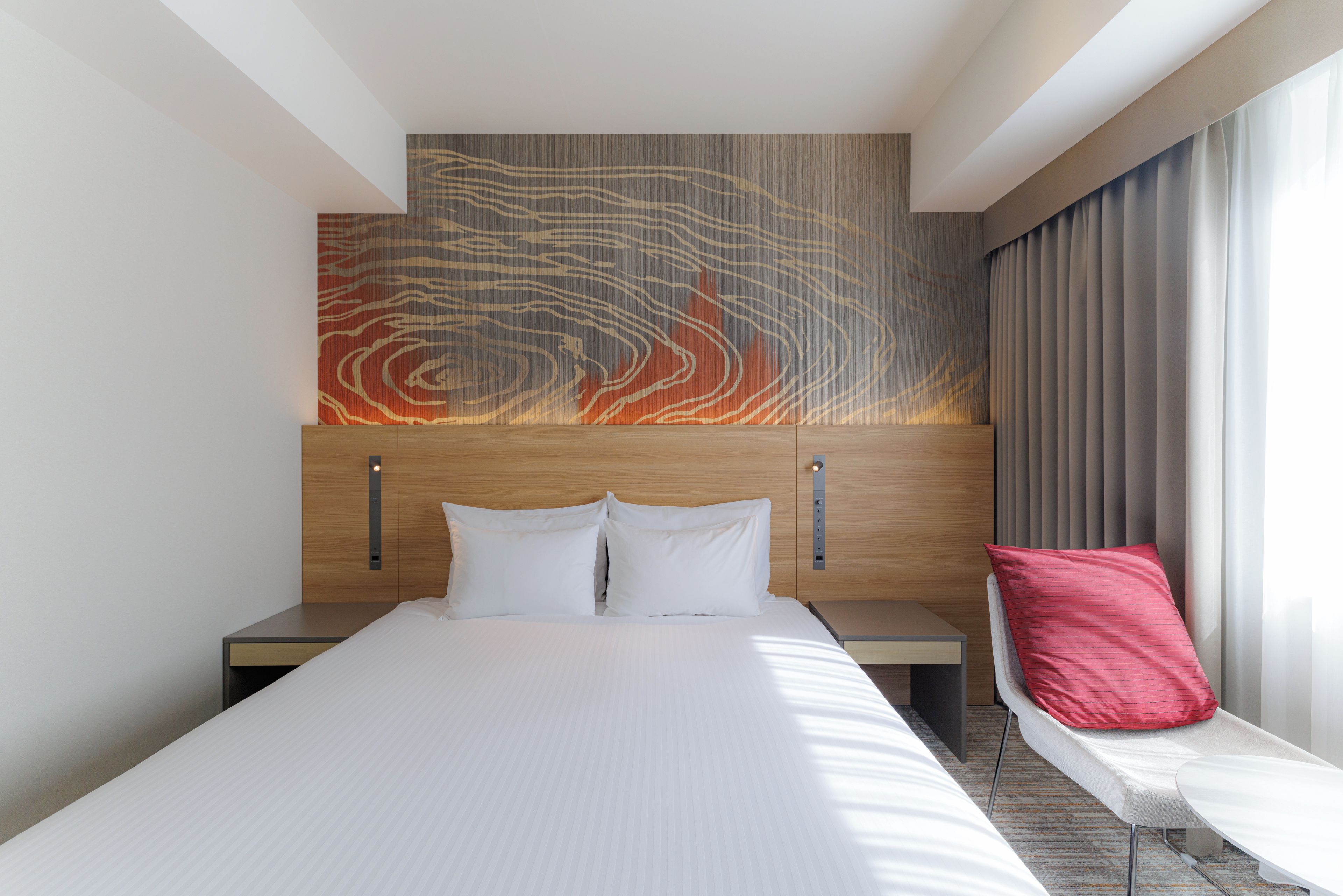 Een moderne hotelkamer met een groot bed, een hoofdeinde met textuurrijke wanddecoratie, een nachtkastje en een raam met gordijnen.