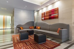 A modern lobby with a grey sofa, black side tables, and a patterned rug.