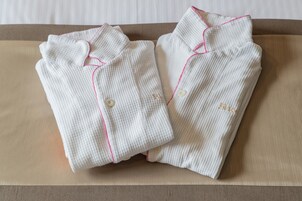 Dos camisas blancas impecablemente dobladas, con detalles rosados en el borde y los botones, sobre una superficie de madera.