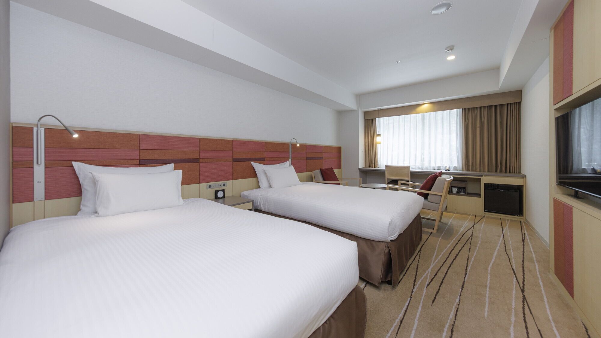 A hotel room with two beds, a TV, a desk, and a window with curtains.