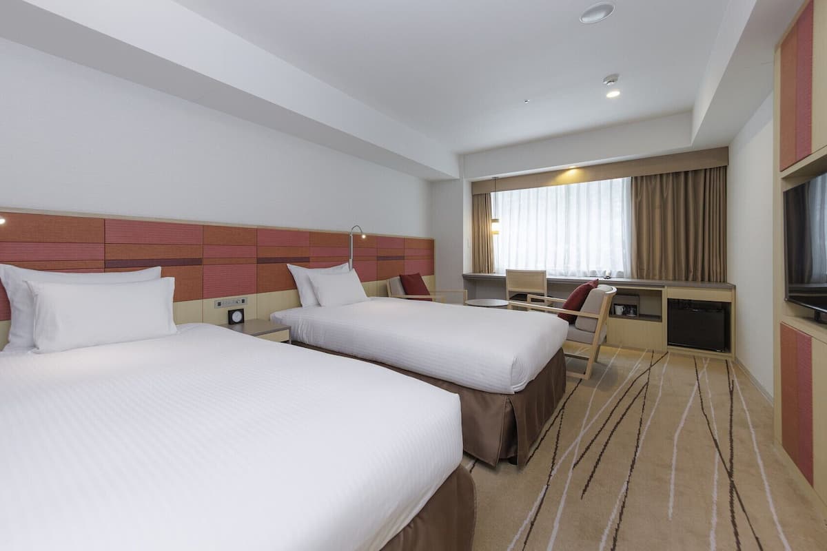 A hotel room with two beds, a TV, a desk, and a window with curtains.