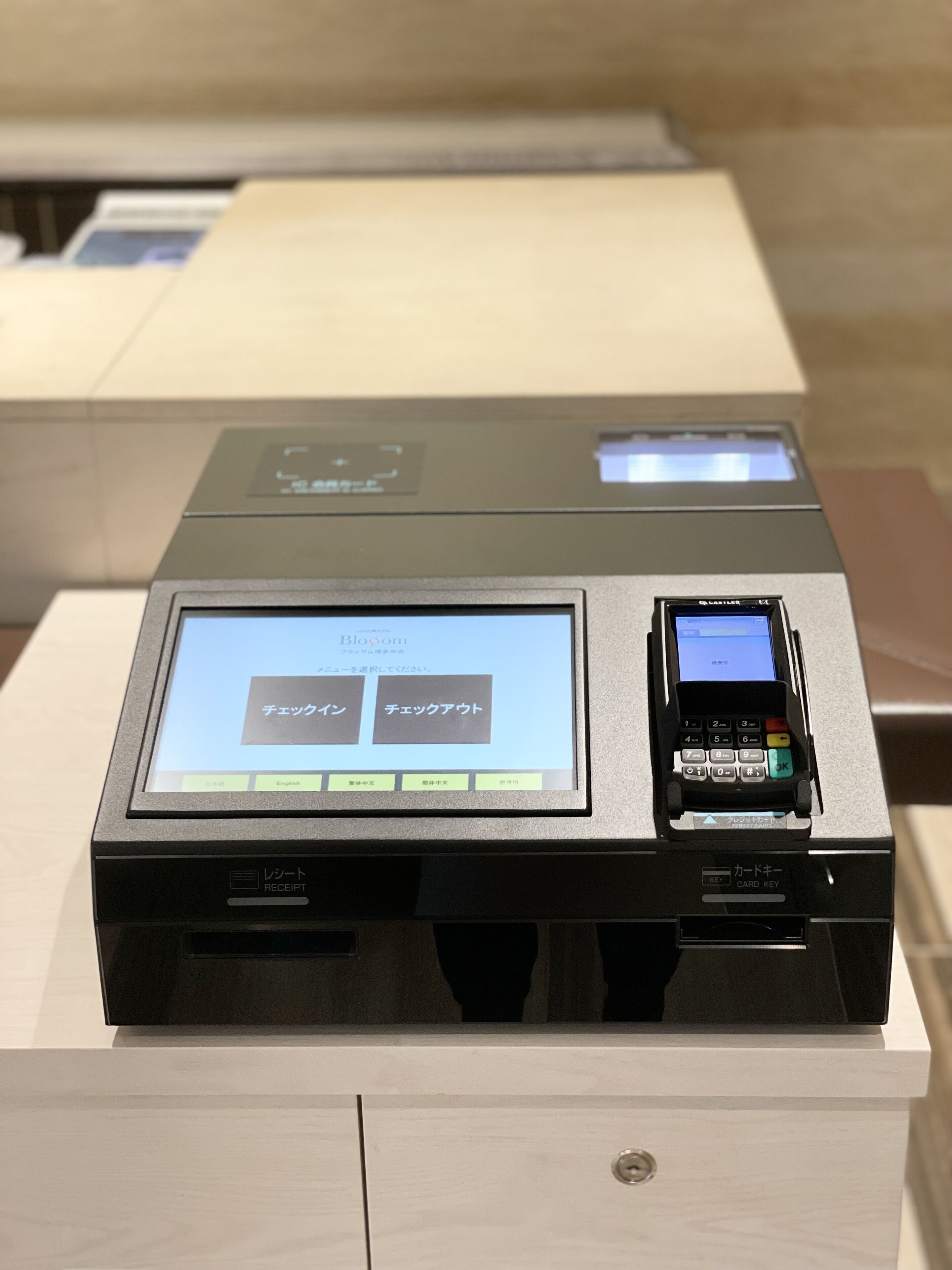 Un terminal de paiement doté d’un écran affichant du texte en japonais, d’un lecteur de cartes et d’une imprimante de reçus.