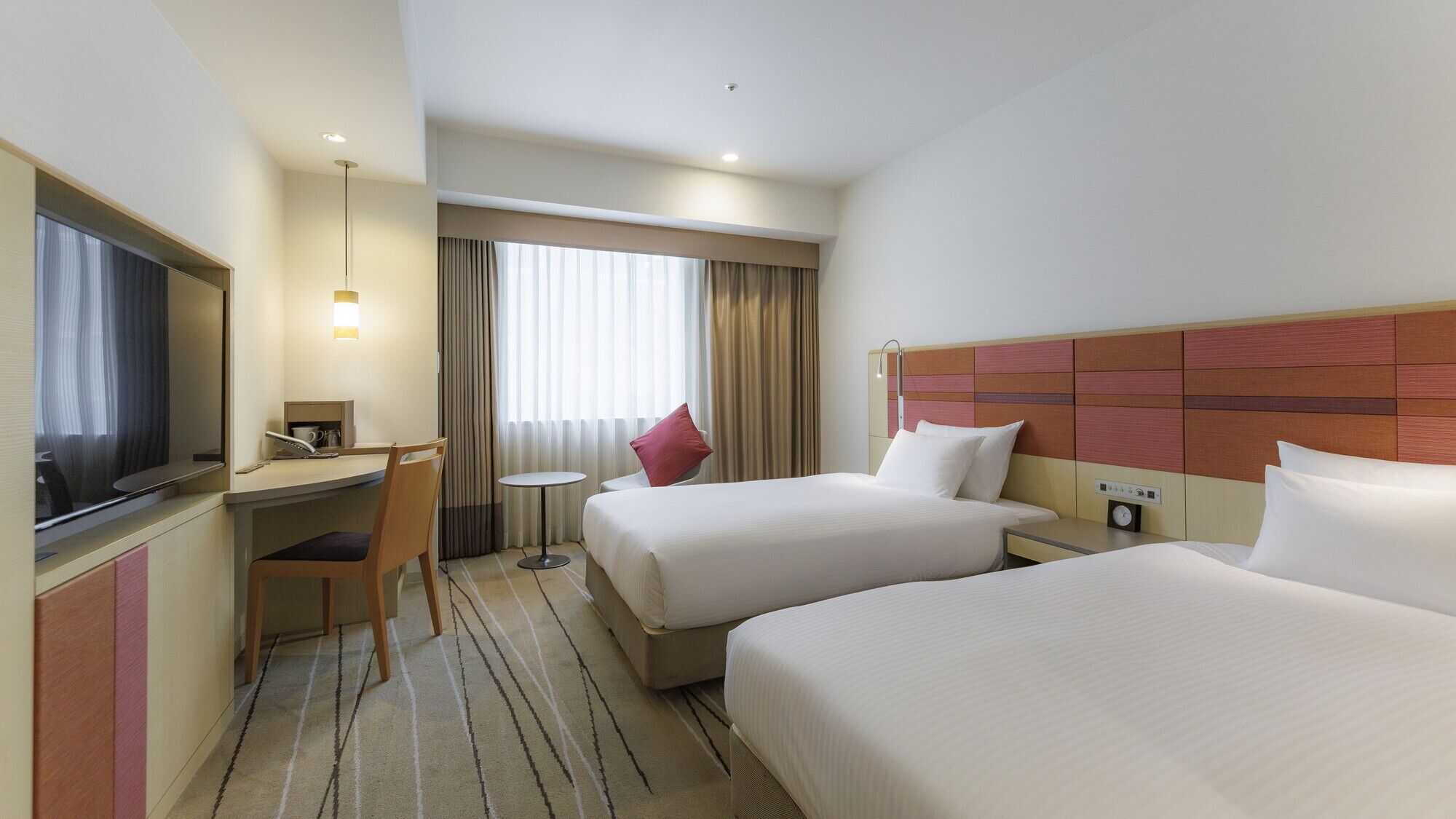 A hotel room with two beds, a desk, a chair, a TV, and a window with curtains.