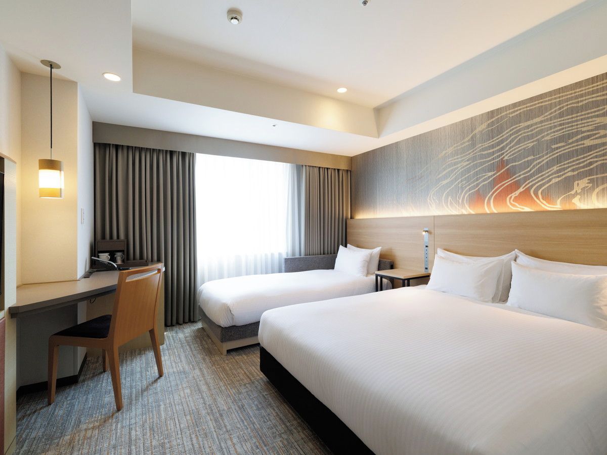 A hotel room with two beds, a desk, a chair, a nightstand, and a large painting on the wall.