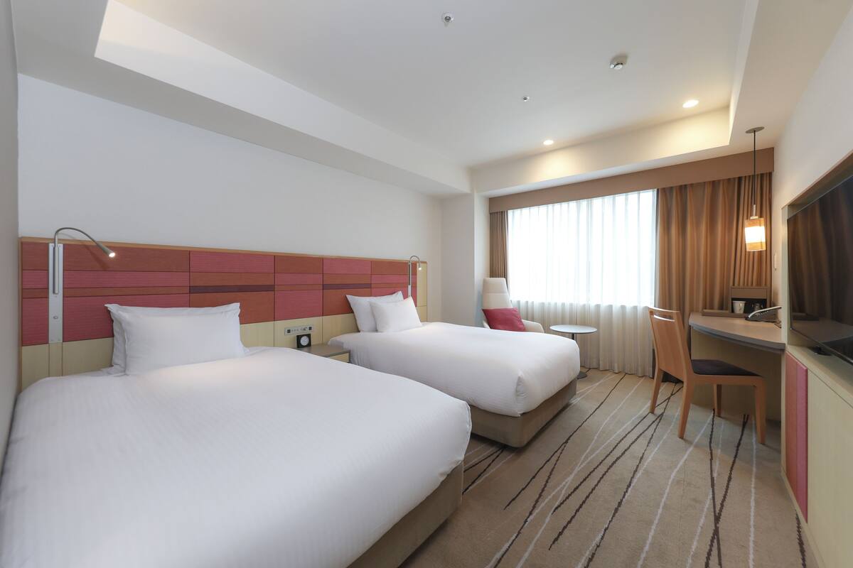 A hotel room with two beds, a desk, and a chair.