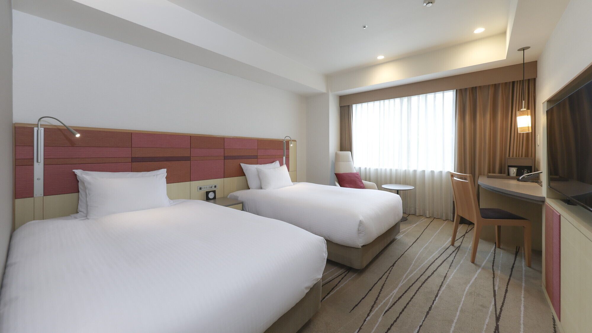 A hotel room with two beds, a desk, a chair, a TV, and a window with curtains.