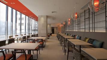A modern restaurant with long tables and benches, large windows, and decorative lighting.