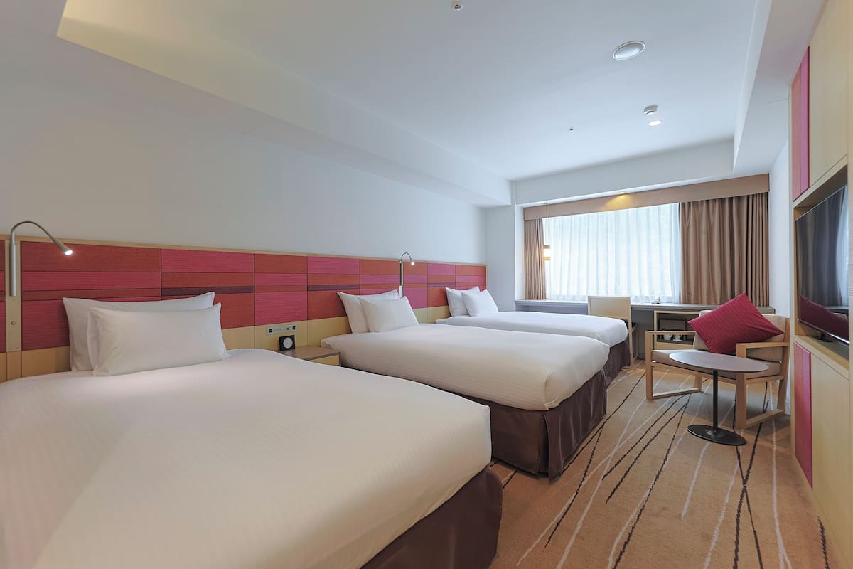 A hotel room with three beds, a desk, a chair, and a TV.