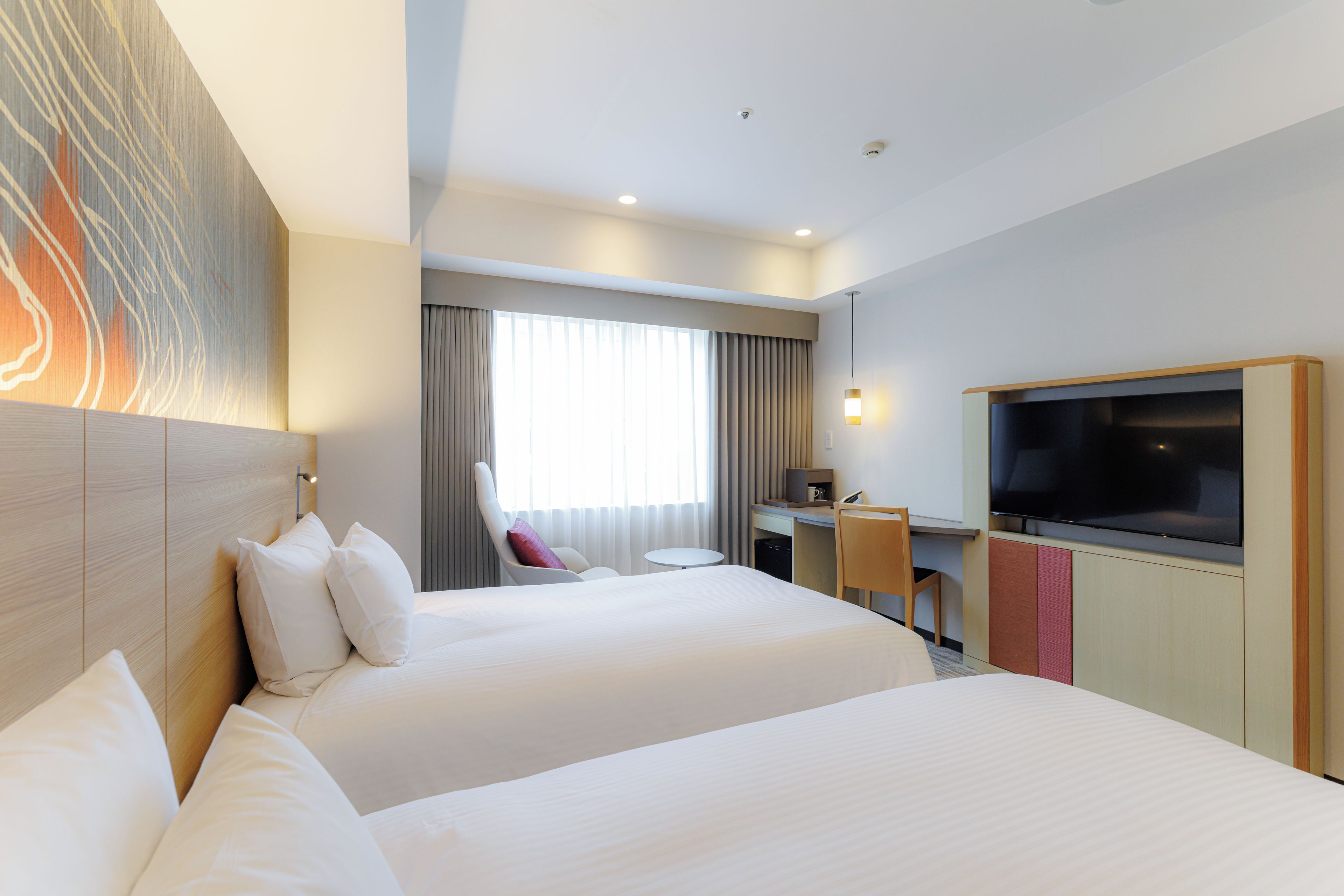 A hotel room with two beds, a desk, a chair, a television, and a large window with curtains.