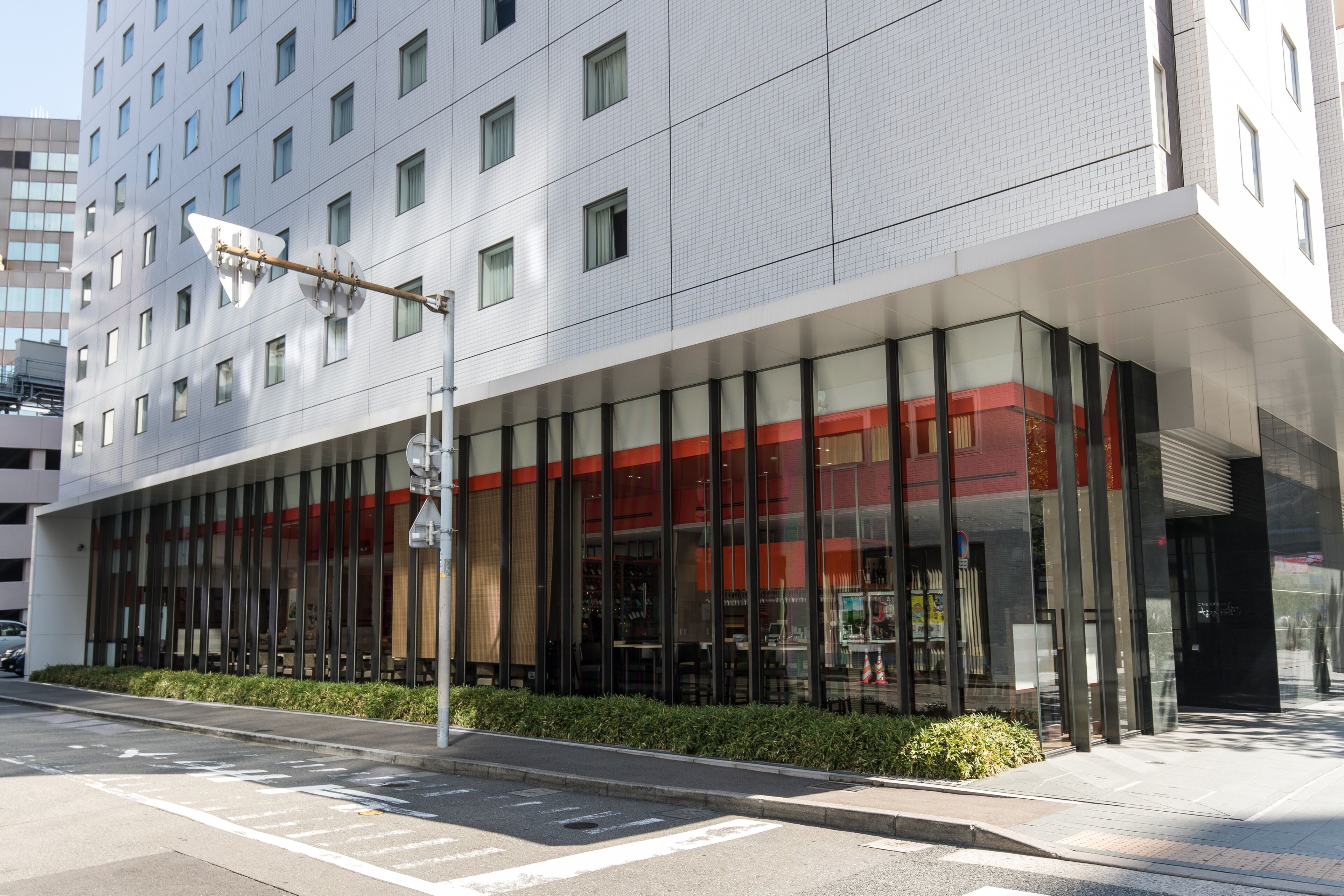 A modern building with a glass facade, a red accent wall, and a clear view of the interior through the windows.
