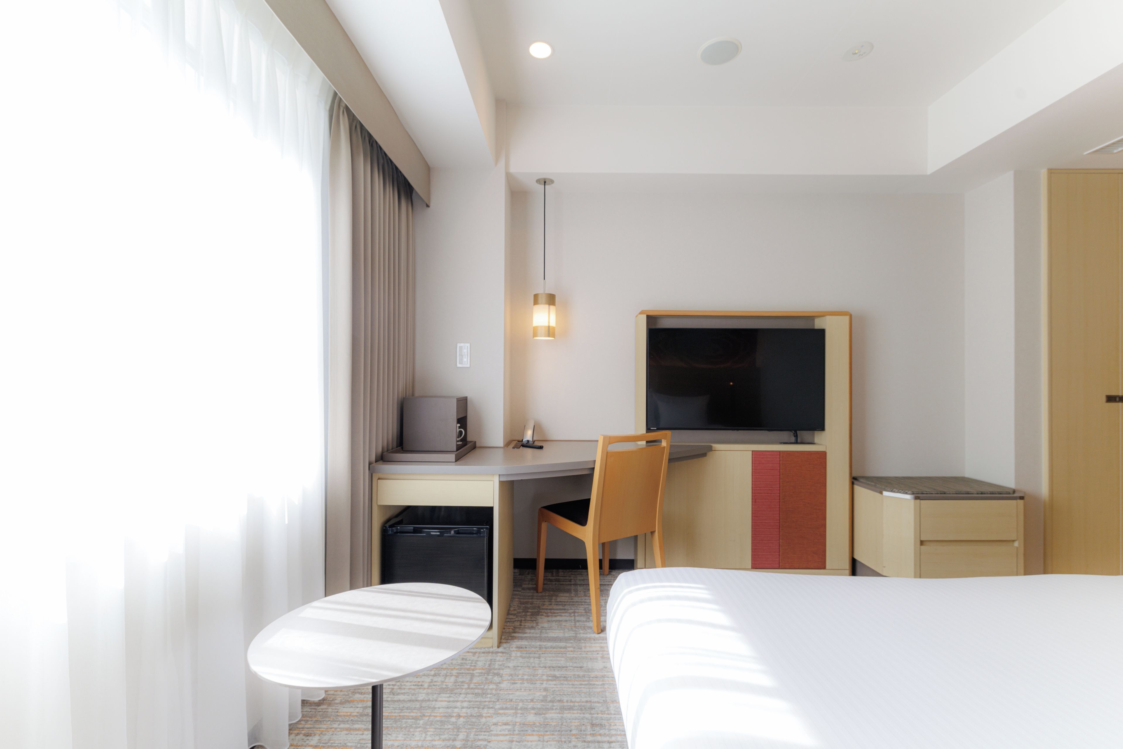 Une chambre d’hôtel avec un lit, un bureau, une chaise, une télévision et une petite table.