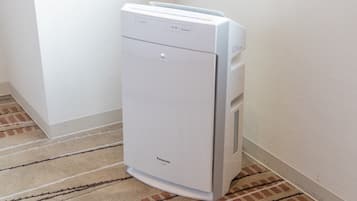 A white Panasonic air purifier in a corner of a room with a patterned carpet.