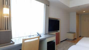 A hotel room with a desk, chair, TV, bed, and a window with curtains.
