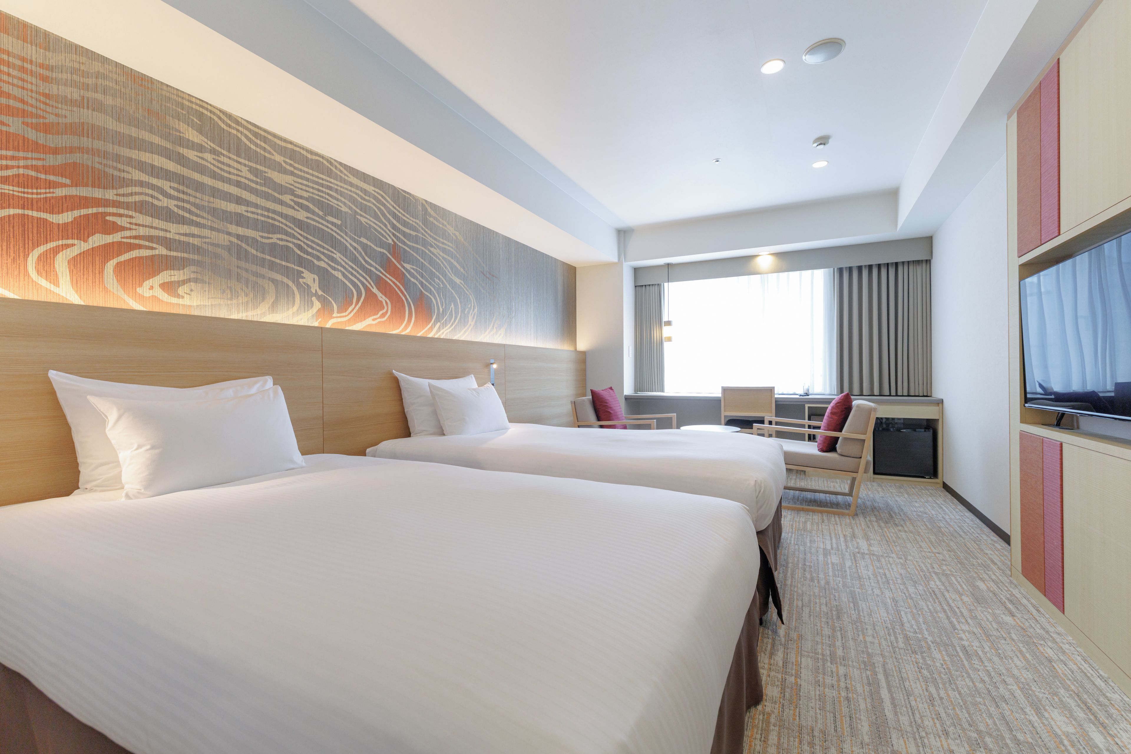 Ein Hotelzimmer mit zwei Betten, einem großen Wandbild, einem Fernseher und einer Sitzecke mit Blick ins Freie.