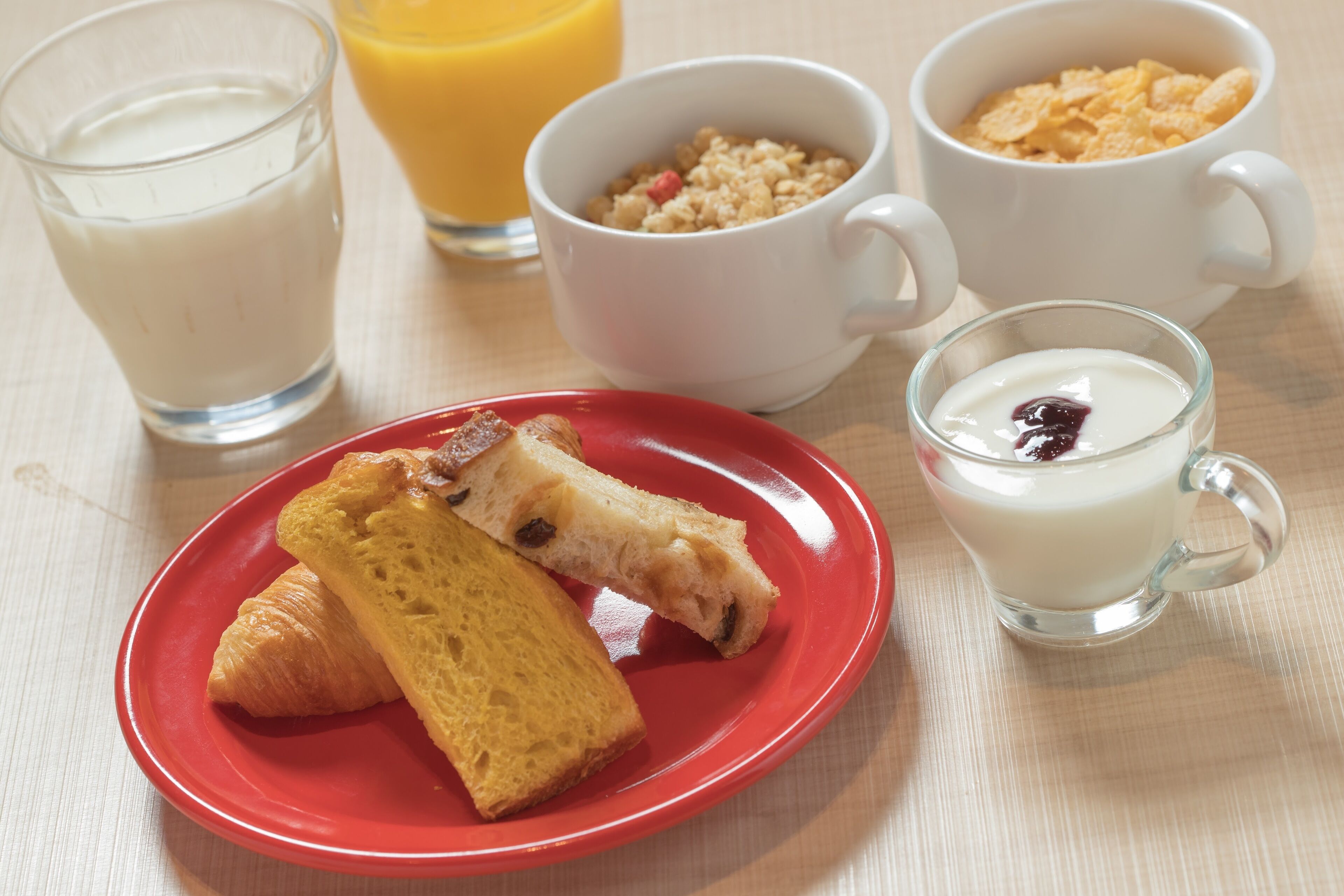 A breakfast setting with croissants, cereal, milk, and orange juice on a table.