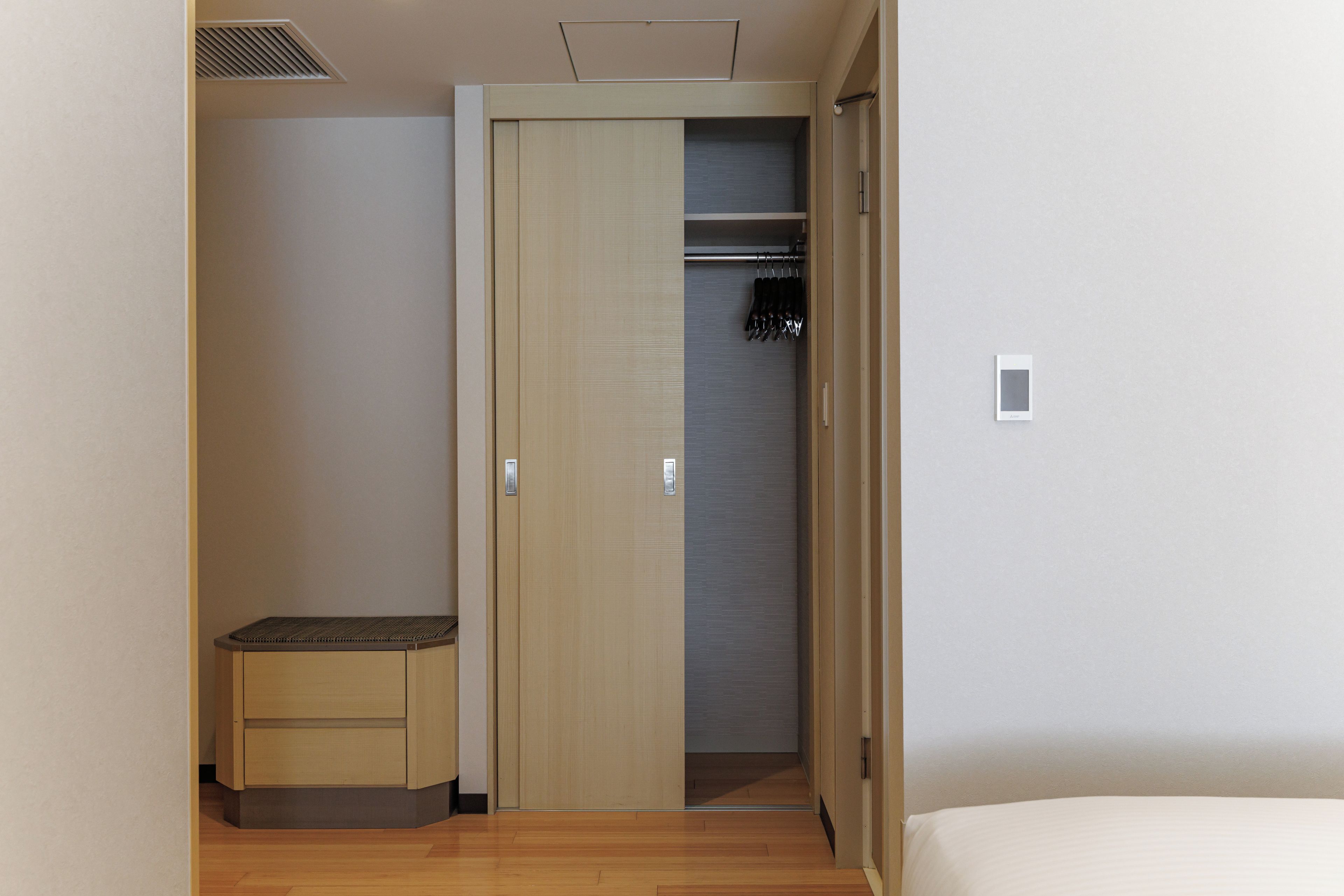 Een slaapkamer met een houten vloer, een bed, een kledingkast en een klein bankje.