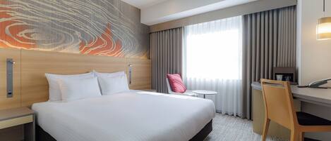 Quarto de hotel com cama grande, escrivaninha, cadeira e vista para o exterior pela janela.