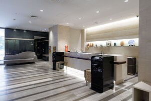 A modern hotel lobby with a reception desk, seating area, and a wall with decorative items.