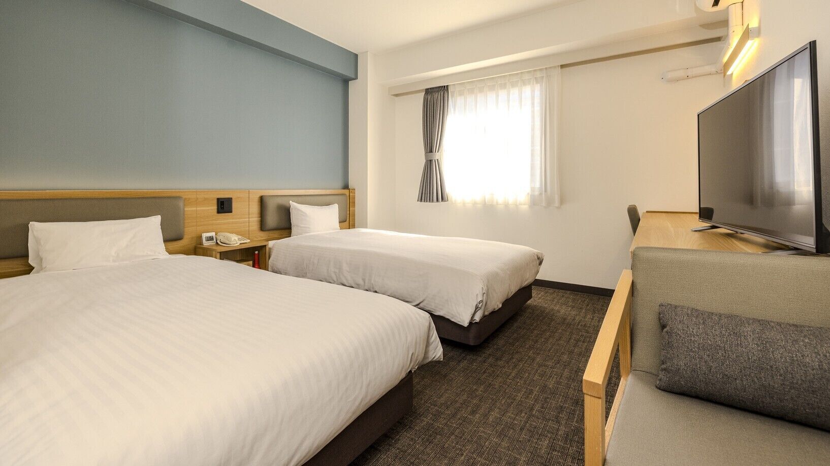A hotel room with two beds, a TV, a desk, and a sofa.