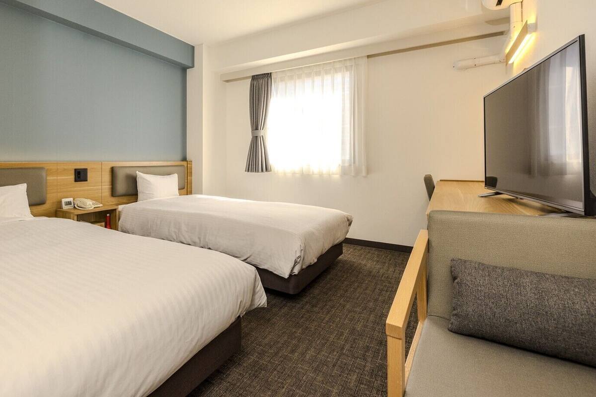 A hotel room with two beds, a TV, a desk, and a sofa.