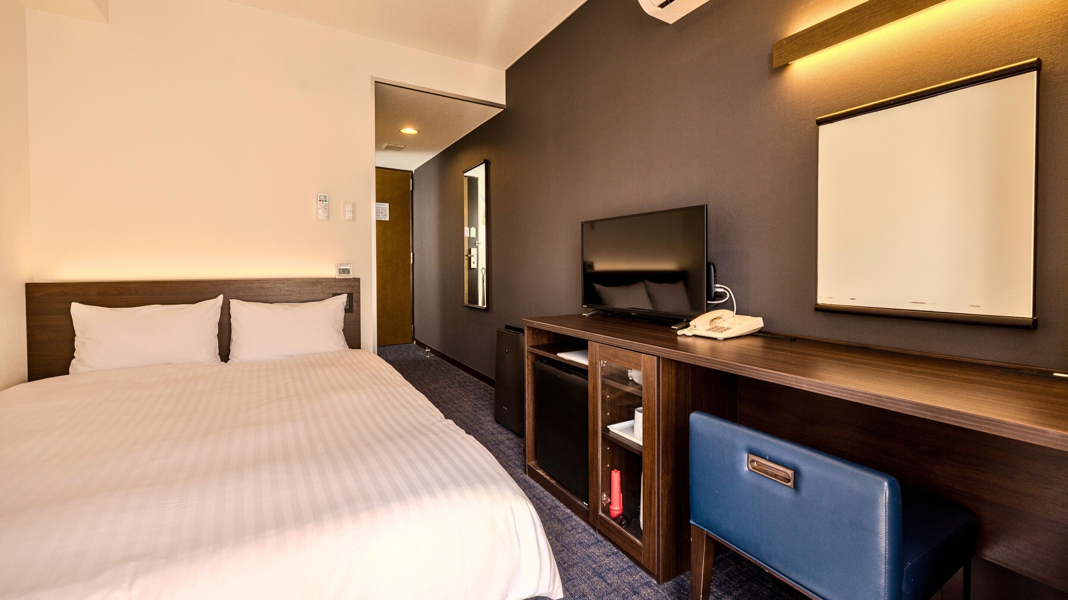Une chambre d’hôtel équipée d’un lit, d’une télévision, d’un bureau avec un téléphone et d’un miroir.